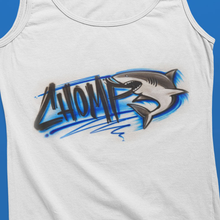 White tank top with airbrushed graffiti-style lettering that says “CHOMP” and a detailed shark illustration biting through the design, with blue streaks and shading.