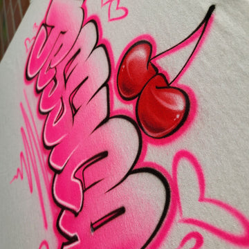 Custom airbrush shirt with bold pink bubble graffiti lettering, surrounded by hearts, sparkles, and topped with a red cherry design.
